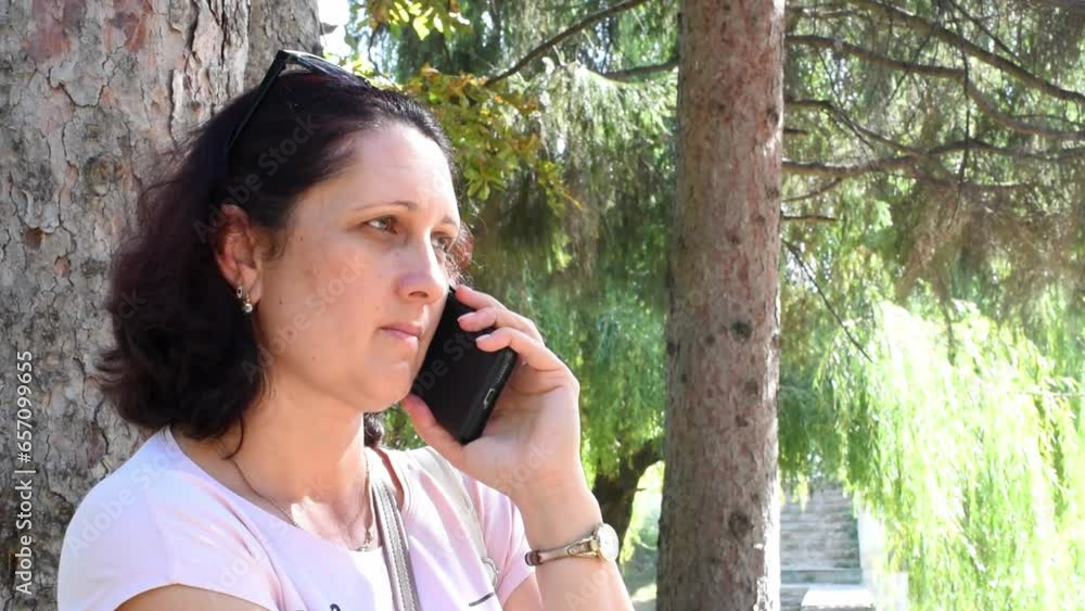 Serious woman talks on the phone in the park, unpleasant conversation. horizontal 4k footage Serious woman talks on the phone in the park, unpleasant conversation. horizontal 4k footage