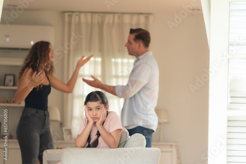 Annoyed and unhappy young girl look at camera, trapped in middle of tension by her parent argument in living room. Unhealthy domestic lifestyle and traumatic childhood develop to depression.Synchronos