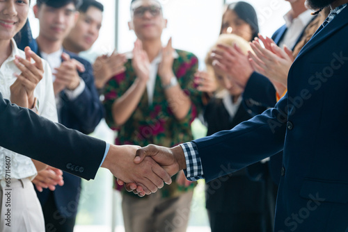 Cropped image of businessmen shaking hand and making a contract in the sign of agreement, cooperation rounded with smiling employees clapping hands and applause behind. Front view. Intellectual.