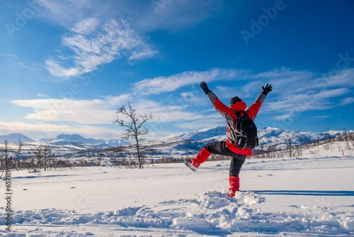 Sporty person in red sport jacket enjoys snow and breathtaking Norwegian landscape. Sunny winter activity.