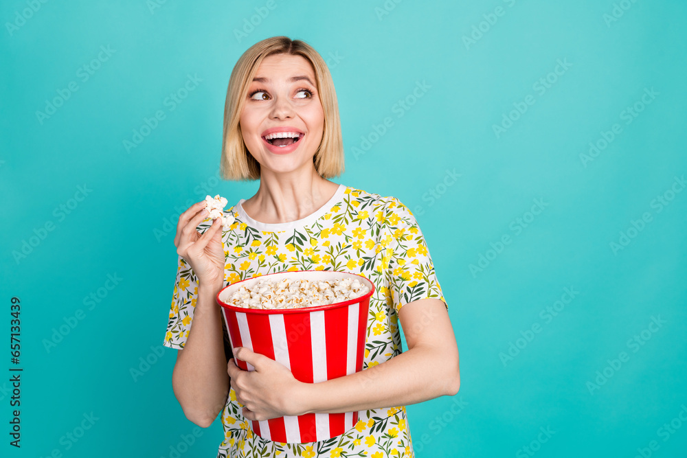 Photo of cheerful excited lady wear flower print t-shirt eating pop corn looking empty space isolated turquoise color background