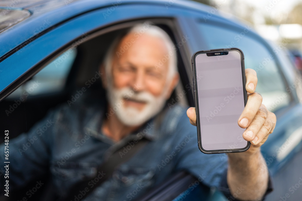 Cropped shot of a senior man driving a car and showing the smart phone with blanc screen.