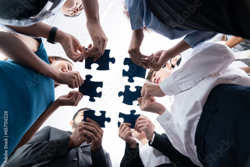 Below view of diverse corporate officer workers collaborate in office connecting puzzle pieces as partnership and teamwork concept. Unity and synergy in business idea by merging jigsaw puzzle. Concord