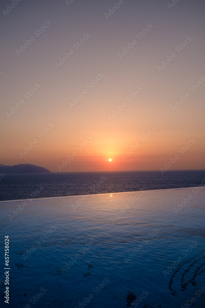 Panoramic view of a swimming pool overlooking the Aegean Sea and a breathtaking sunset in Ios Greece
