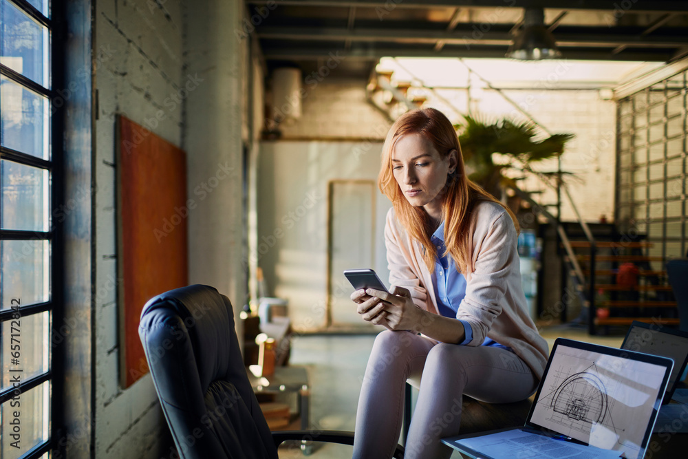 Fototapeta premium Young Caucasian female designer using her smartphone while working in startup company office