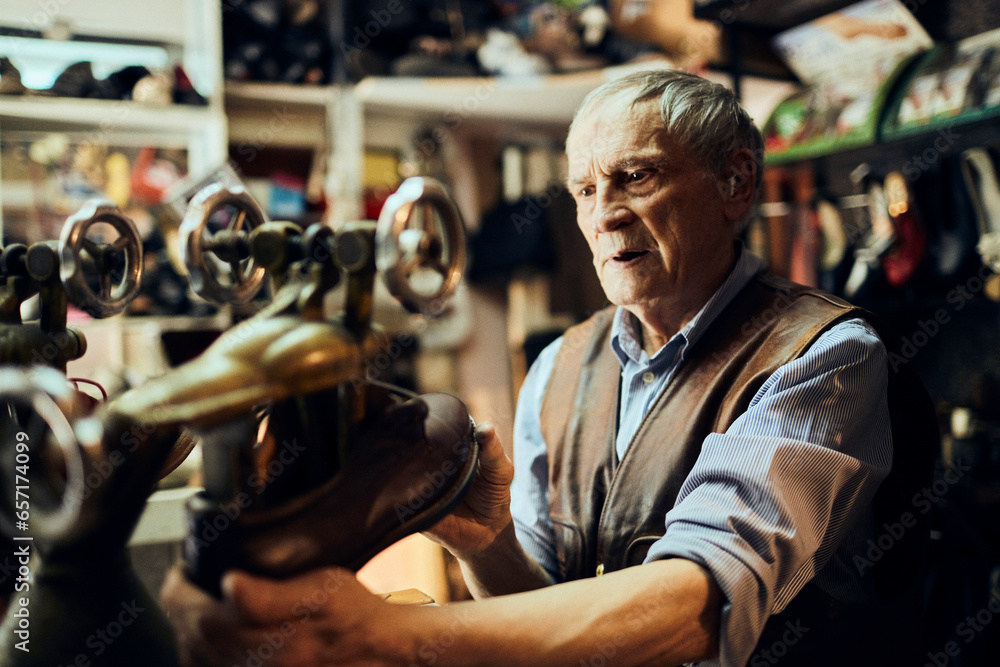 Obraz premium Senior male shoemaker restoring a shoe in his old workshop in the city