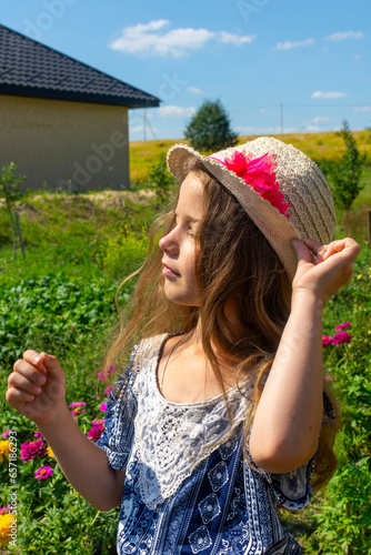 A pretty caucasian girl in a straw hat relaxing among the greenery on a sunny summer day. Happy childhood.