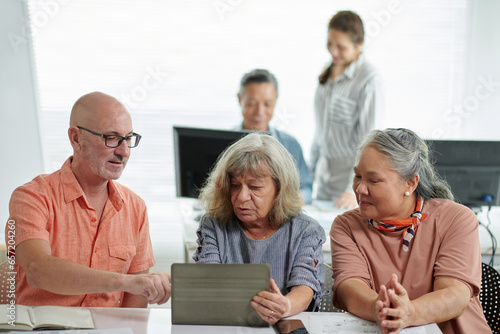 Mature man helping classmates to install application on tablet computer