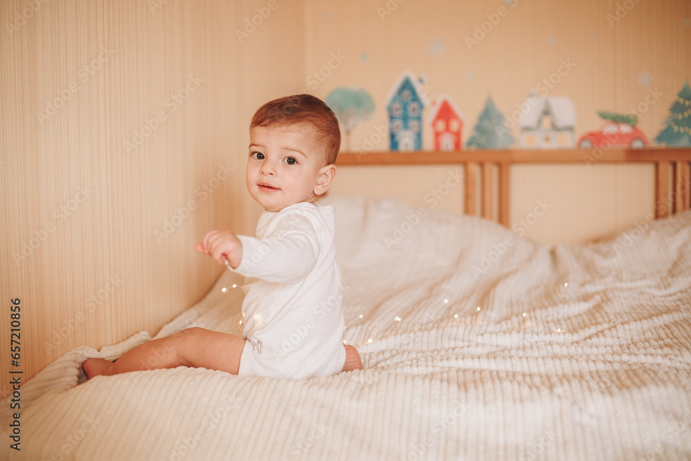 A little baby in a white bodysuit playing with lights sitting on a bed A little baby in a white bodysuit playing with lights sitting on a bed