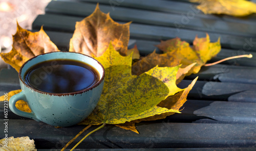 A blue cup of coffee stands on a park bench, yellow foliage, autumn mood.