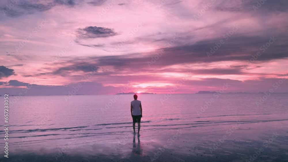 Rear view young happy man opening arms looking at ocean at beautiful sunset time on tropical beach. Freedom, happiness or success concept. Male tourist enjoying freedom on paradise island in the Ocean Rear view young happy man opening arms looking at ocean at beautiful sunset time on tropical beach. Freedom, happiness or success concept. Male tourist enjoying freedom on paradise island in the Ocean
