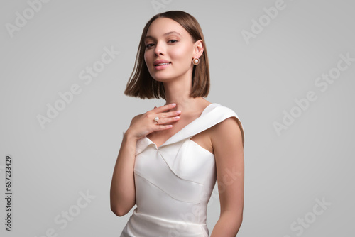 Close up portrait of a beautiful elegant woman with stylish jewelry on a white gray background. Girl in white dress