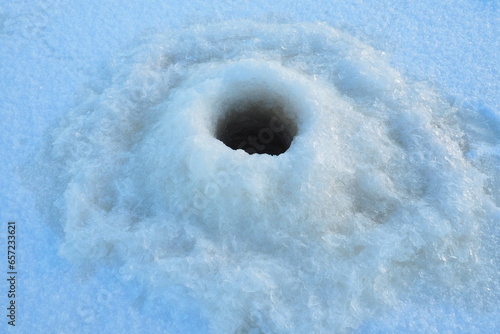 Winter fishing in January. A round hole in the ice and snow, made with an ice pick. Hobby, sports or amateur fishing. Danger of falling into cold water. Brittle ice photo