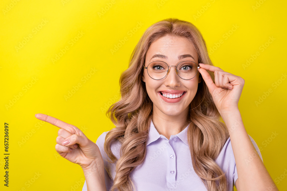 Photo of sweet pretty woman dressed violet t-shirt hand eyewear showing finger empty space isolated yellow color background Photo of sweet pretty woman dressed violet t-shirt hand eyewear showing finger empty space isolated yellow color background