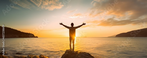 Young man arms outstretched by the sea at sunrise enjoying freedom and life, people travel wellbeing concept