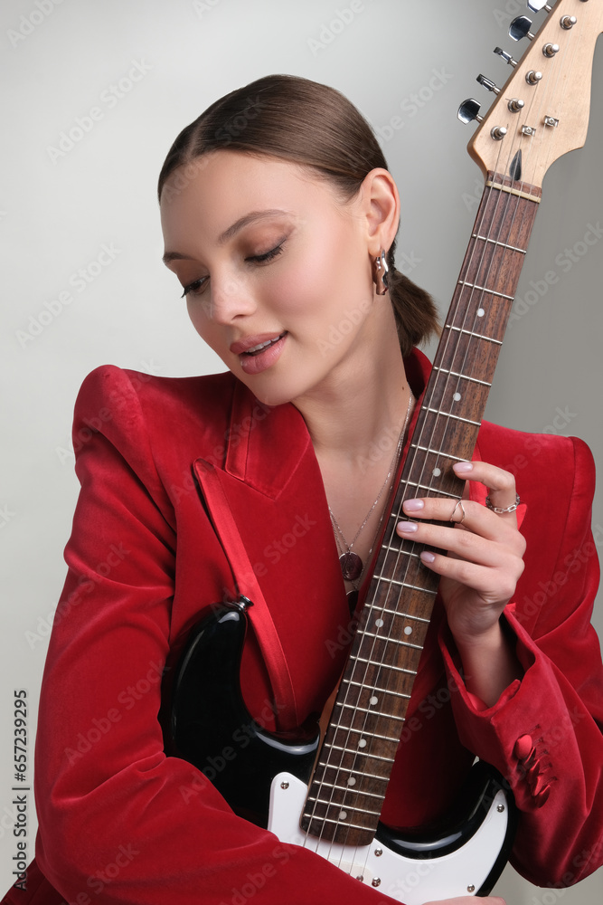 Close up portrait of a beautiful elegant woman with stylish jewelry on a white gray background. Girl in red blazer keep guitar Close up portrait of a beautiful elegant woman with stylish jewelry on a white gray background. Girl in red blazer keep guitar