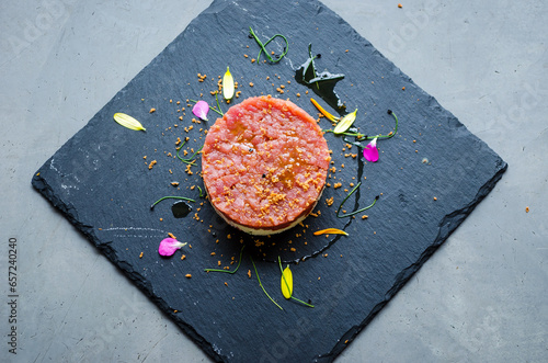 Gourmet tuna tartare beautifully garnished with edible flowers and herbs, served on a sleek black slate plate for an elegant presentation