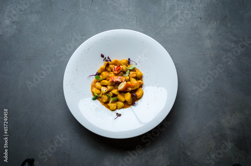 Vibrantly colored plate of handmade gnocchi with lobster, tomato, and herbs on a gray industrial-style background