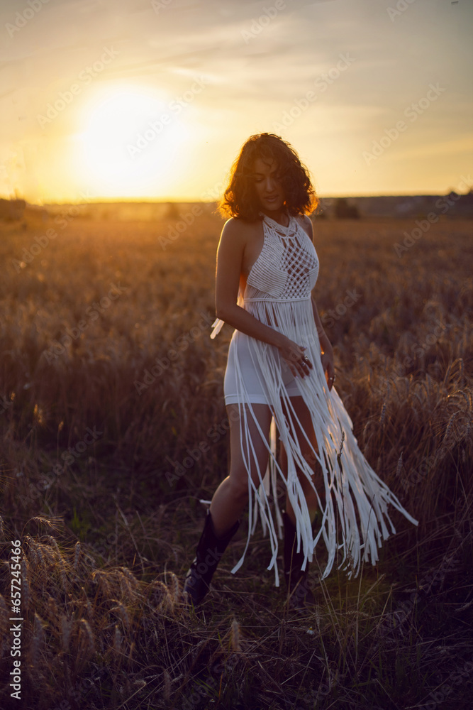 fashion portrait of a curly-haired woman in white clothes dress stand on a field with dry grass in autumn.