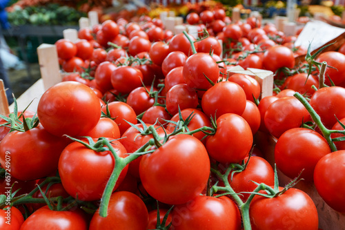 Einkaufen auf dem Wochenmarkt: Blick auf Gemüsekisten mit leckeren und roten Tomaten an einem Verkaufsstand draußen mit Menschen im verschwommenen Hintergrund, selektiver Fokus, Copyspace © redaktion93