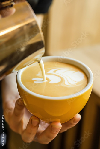 Close-up of barista making cappuccino coffee in coffee shop, hands holding a coffee cup