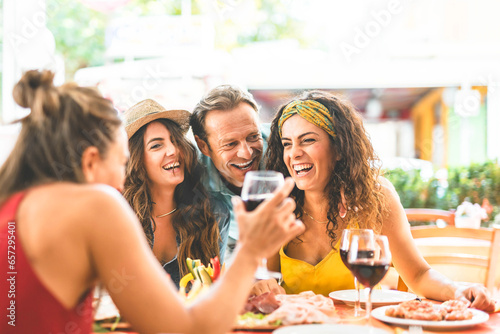 Group of people having fun drinking red wine and dining together sitting outside restaurant terrace-Young friends laughing and enjoying happy hour at pub- Lifestyle Food and beverage concept photo