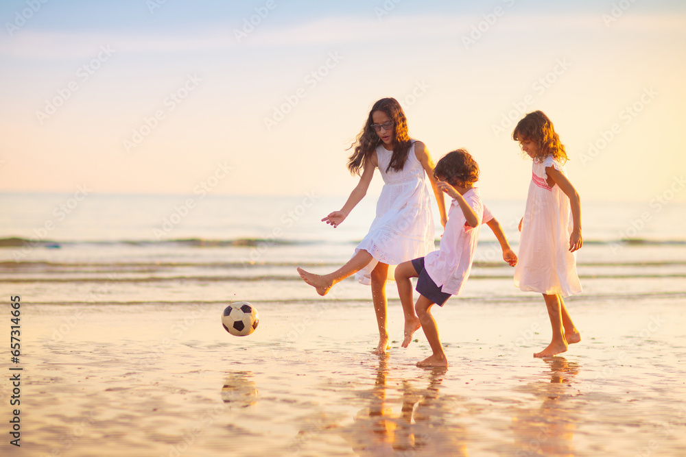 Kids play football on tropical beach at sunset