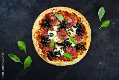 Traditionelle italienische Halloween Spinnen Pizza mit Salami, Mozzarella und Oliven serviert als Draufsicht mit Spinnen und Geister auf einem alten rustikalen Board
