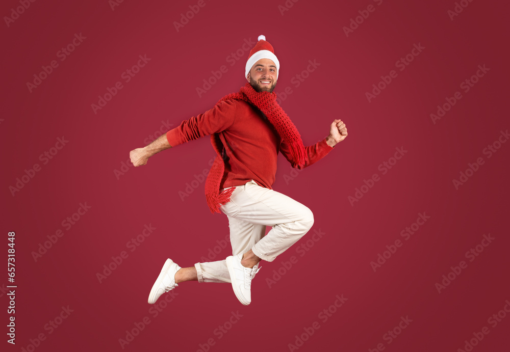 Smiling millennial caucasian guy in Santa hat jumps, frozen in air, enjoy holidays Smiling millennial caucasian guy in Santa hat jumps, frozen in air, enjoy holidays