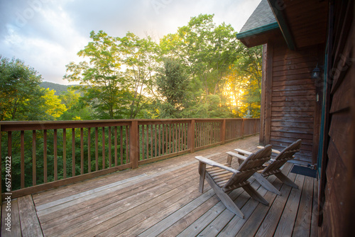 Two wooden adirondack chairs on cabin porch facing the forest overlook