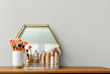 Holder with different makeup products and mirror on dressing table near light wall in room