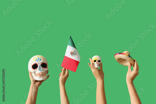 Female hands holding painted skulls, Mexican flag and sombrero on green background