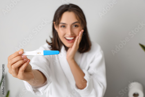 Happy young woman with pregnancy test sitting on toilet bowl in restroom, closeup