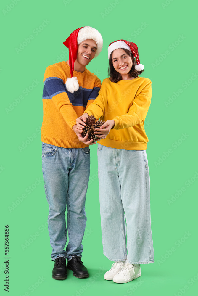 Happy young couple in Santa hats with forest bumps on green background Happy young couple in Santa hats with forest bumps on green background