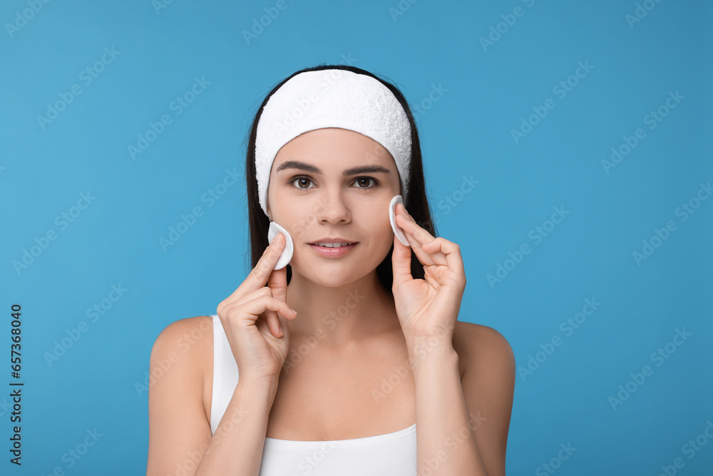 Young woman cleaning face with cotton pads on light blue background Young woman cleaning face with cotton pads on light blue background