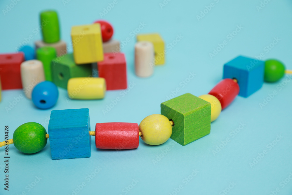 Naklejka premium Wooden pieces and string for threading activity on light blue background, closeup. Educational toy for motor skills development