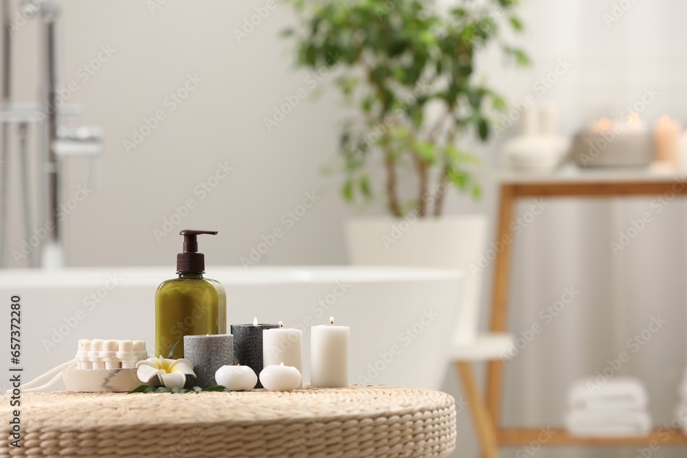 Spa products, burning candles and plumeria flower on wicker table in bathroom. Space for text Spa products, burning candles and plumeria flower on wicker table in bathroom. Space for text