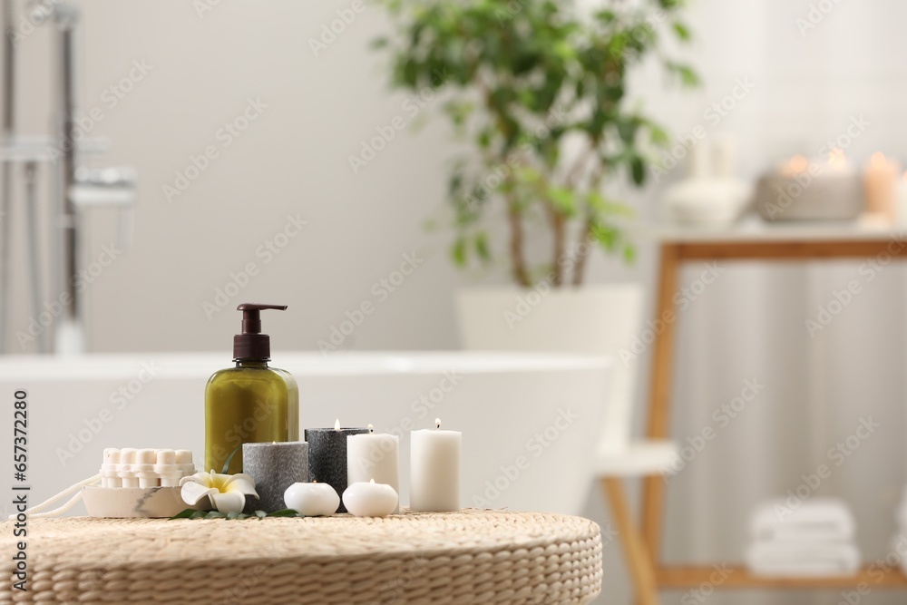 Spa products, burning candles and plumeria flower on wicker table in bathroom. Space for text