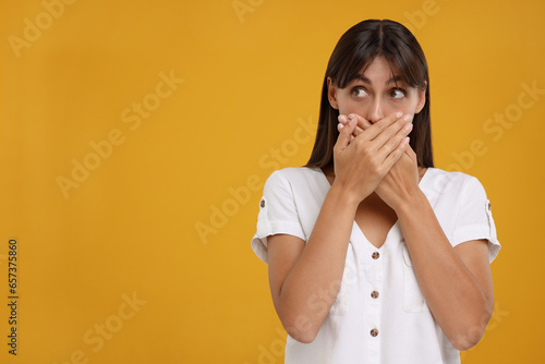 Embarrassed woman covering mouth with hands on orange background, space for text