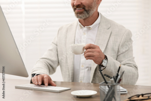 Professional accountant with cup of coffee working at wooden desk in office, closeup