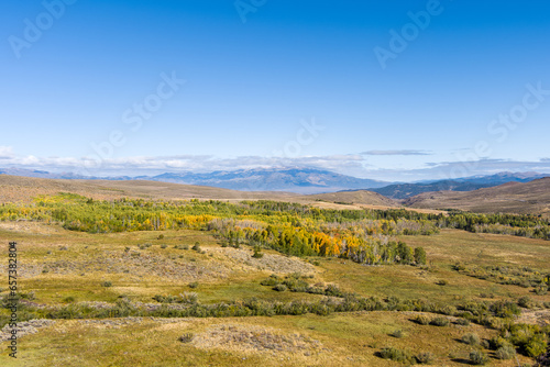 Aerial view of Patches of Autumn colored leaves in the California Eastern Sierras landscape with snow capped mountains small clouds and copy space against a bright blue sky in the background.