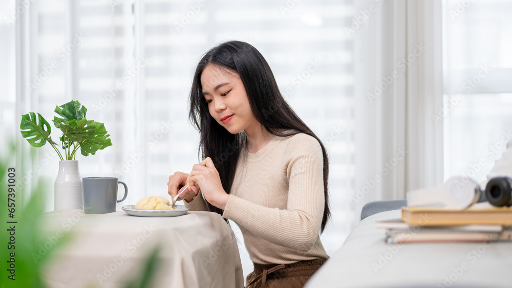 A beautiful and cheerful young Asian woman enjoying her breakfast at a dining table at home. A beautiful and cheerful young Asian woman enjoying her breakfast at a dining table at home.