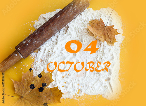 Calendar for October 4: numbers 04, name of the month October in English on scattered flour, next to a rolling pin and maple leaves, yellow background, top view photo