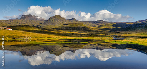 A panorama of a colorful mountain range, tall grass and a generic Icelandic farm house all reflecting on the lake in the foreground
