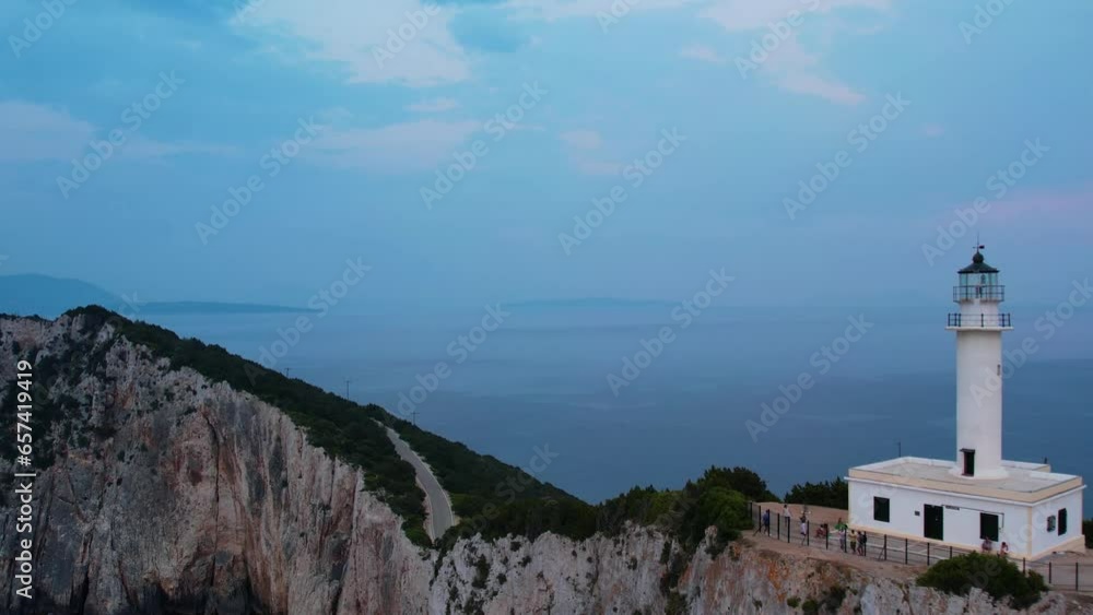 Aerial View Of Doukáto Lighthouse On Cliff Edge Of Lefkada Island With Misty Blue Landscape Sea In Background. Pull back, Establishing Shot Aerial View Of Doukáto Lighthouse On Cliff Edge Of Lefkada Island With Misty Blue Landscape Sea In Background. Pull back, Establishing Shot