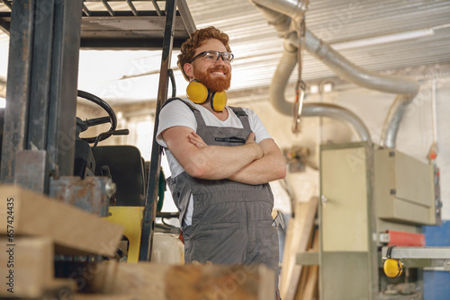 Portrait of smiling carpenter in eyeglasses standing on the background on carpentry workshop