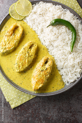 Hilsa fish cooked with mustard and traditional Bangladeshi spices served with white rice closeup on the plate on the table. Vertical top view from above photo