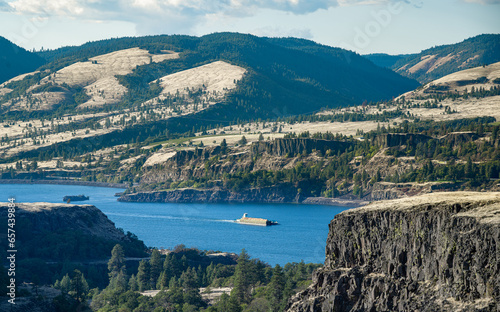A barge filled with wheat for animal feed being pushed by a tugboat upstream in the Columbia River Gorge. Seen from Tom McCall Preserve in Mosier, Oregon