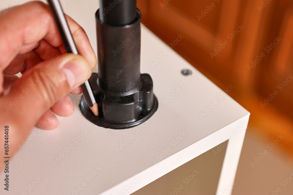 Holes for fastening the furniture leg are marked with a pencil. Assembling cabinet furniture.