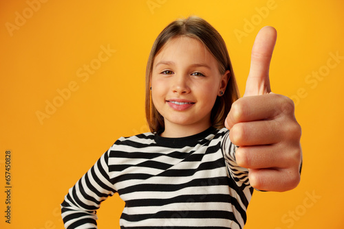Teen girl showing thumb up sign against yellow background